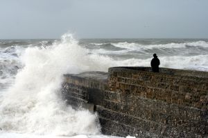a person sitting on a break water in a stormy sea